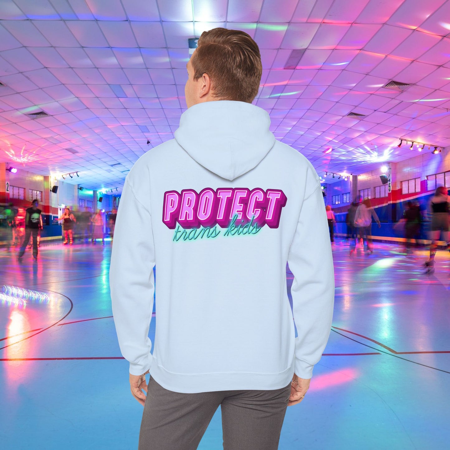 A person is at a roller skating rink, sporting a high-quality Protect Trans Kids Hoodie from Printify, crafted from ethically grown cotton, with "PROTECT trans kids" boldly and colorfully emblazoned on the back. The rink is bathed in vibrant, colorful lights, and other skaters can be seen gliding in the background.