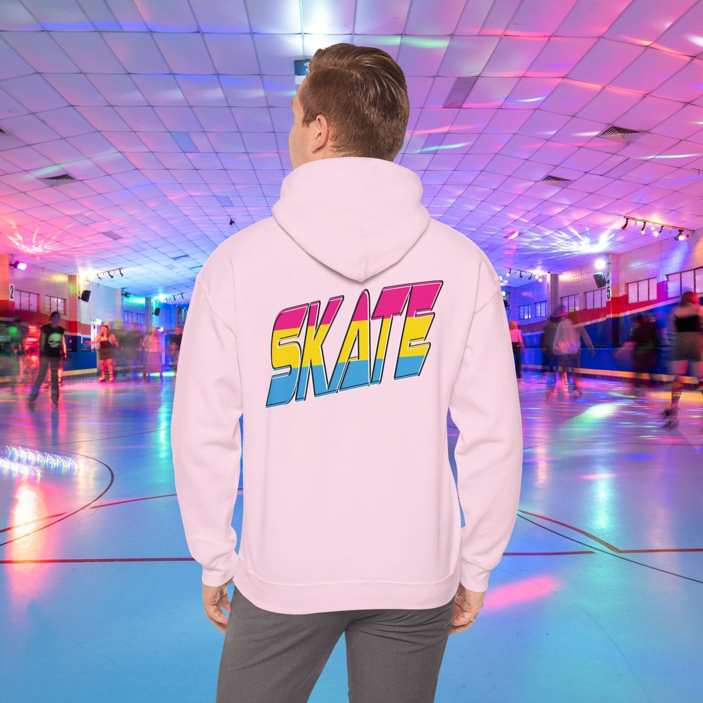 A person wearing a high-quality SKATE Pansexual Pride Hoodie by Printify, featuring the word "SKATE" in large, colorful letters, stands in a vibrant roller skating rink. The unisex heavy blend hoodie is part of a trans and queer-owned brand. The rink is decorated with colorful lights, and people are skating in the background as the person faces away from the camera.