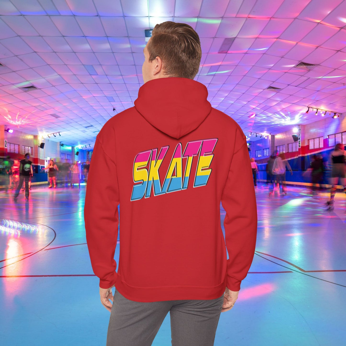 A person wearing a high-quality SKATE Pansexual Pride Hoodie by Printify, featuring the word "SKATE" in large, colorful letters, stands in a vibrant roller skating rink. The unisex heavy blend hoodie is part of a trans and queer-owned brand. The rink is decorated with colorful lights, and people are skating in the background as the person faces away from the camera.