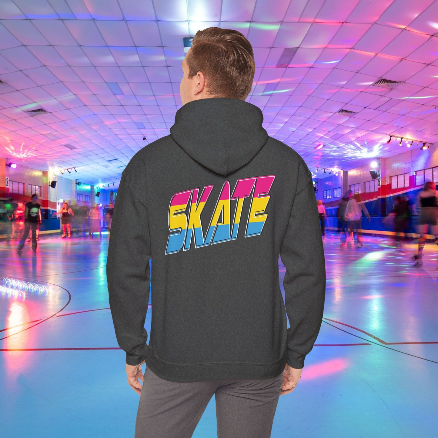 A person wearing a high-quality SKATE Pansexual Pride Hoodie by Printify, featuring the word "SKATE" in large, colorful letters, stands in a vibrant roller skating rink. The unisex heavy blend hoodie is part of a trans and queer-owned brand. The rink is decorated with colorful lights, and people are skating in the background as the person faces away from the camera.