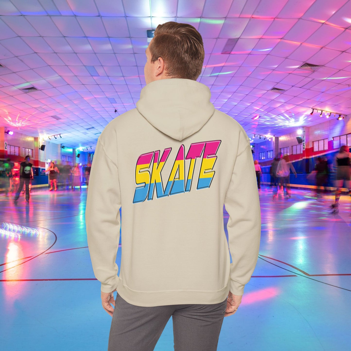 A person wearing a high-quality SKATE Pansexual Pride Hoodie by Printify, featuring the word "SKATE" in large, colorful letters, stands in a vibrant roller skating rink. The unisex heavy blend hoodie is part of a trans and queer-owned brand. The rink is decorated with colorful lights, and people are skating in the background as the person faces away from the camera.