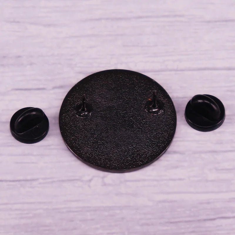 The Ally enamel pin featuring the progress pride flag is a round black enamel pin with two pointed posts and black pin backs, displayed on a light wooden surface—ideal for your pride collection.