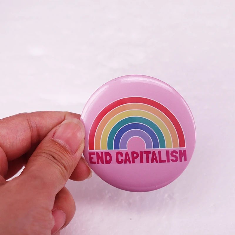 A vibrant "End Capitalism - Pink Rainbow Button Badge" is held against a white background, making a bold statement with its activism and pride message.