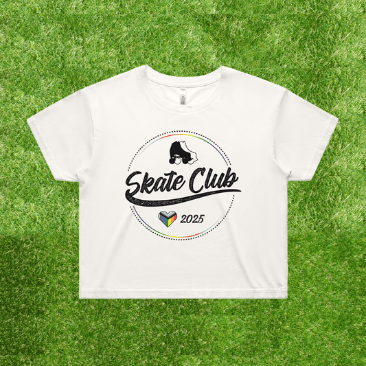 Introducing the NEW!! SKATE CLUB 2025 progress pride crop tee by Gay Skate. This white tee features the Skate Club 2025 logo with stylized text and an illustration of a skateboarder. Below, it incorporates a vibrant heart design that subtly captures the essence of Gay Skate's inclusive vibe, all presented against a natural grassy backdrop for a touch of style and embrace of inclusivity.