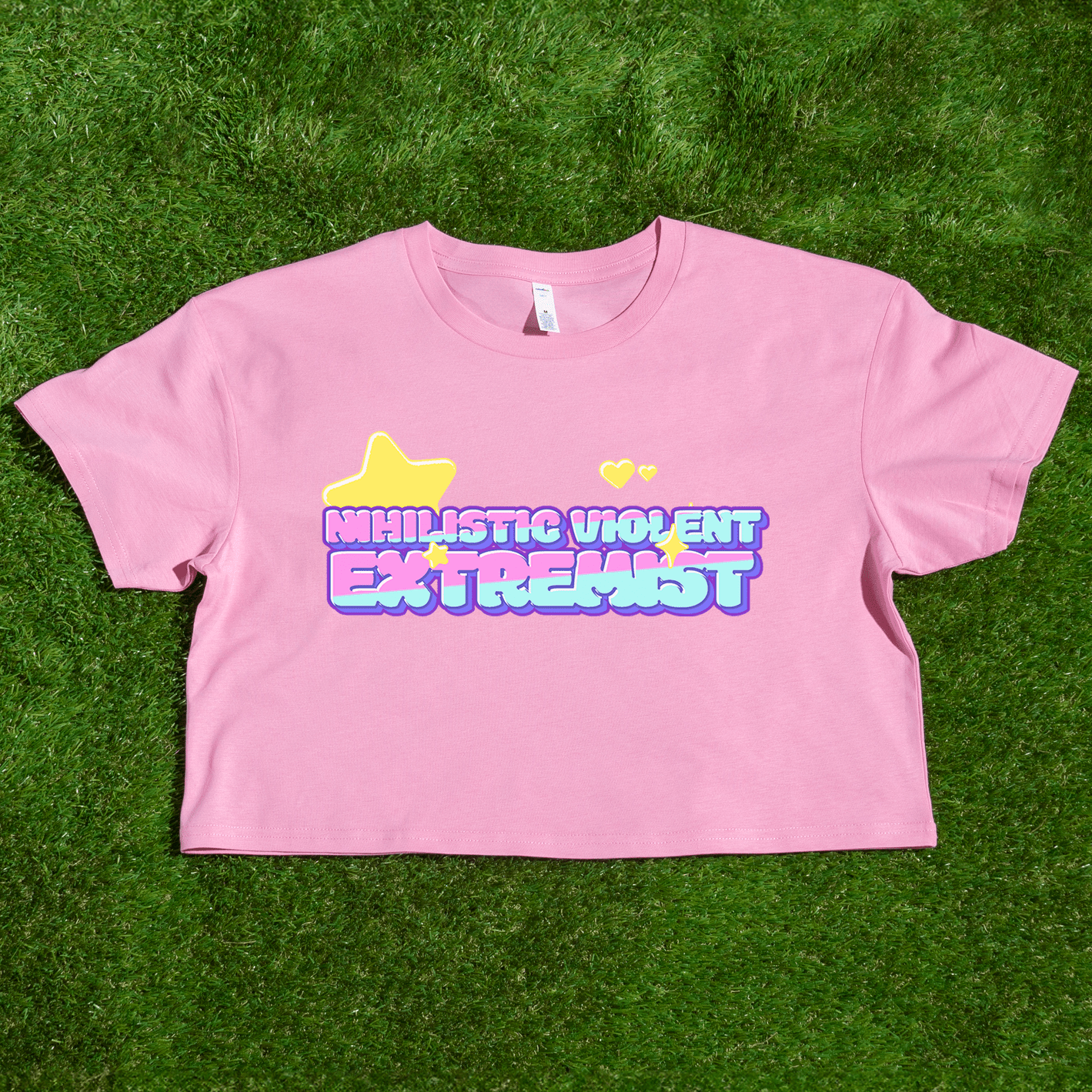 The Nihilistic Violent Extremist locally printed satire crop tee is a pink top with colorful bubble text, a yellow star, and two hearts, designed by a trans and queer owned brand