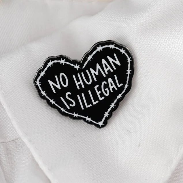 Heart-shaped badge with 'No Human Is Illegal' text on a white shirt