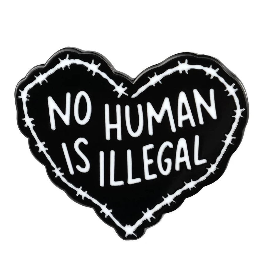Heart-shaped enamel pin with 'No Human Is Illegal' text surrounded by barbed wire on a white background