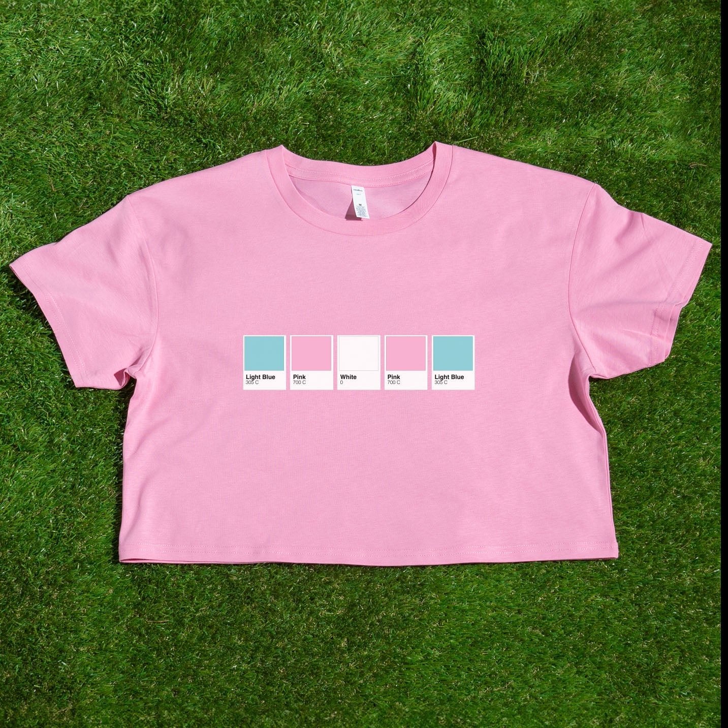 A pink crop tee, locally printed by a queer-owned business, features five color swatches labeled Light Blue, Pink, White, Pink, and Light Blue in a pride flag-inspired design. Pantone pride flag crop tee: Rainbow, Trans, Non-binary & more.