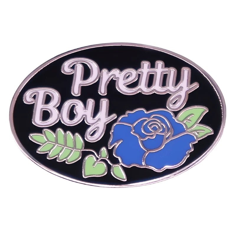 The pin, named "Pretty Boy Enamel Pin" by the brand Gay Skate, features the words in white lettering against a black background. Below the text is a blue rose detail with green leaves surrounding it. Perfect for twinks, gays, mascs, bois and other transgender and non-binary people.45488150282395