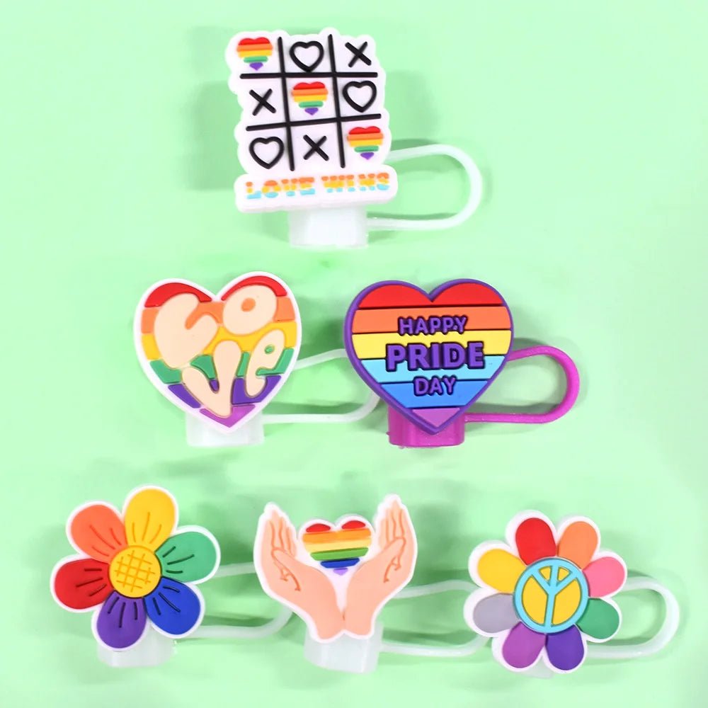 Pride straw toppers, designed for Stanley Cup straws, feature colorful charms. Designs include Rainbow Pride with tic-tac-toe boards and rainbows, a "LOVE" heart, a "HAPPY PRIDE DAY" badge, hands holding a rainbow heart, and a peace symbol flower.