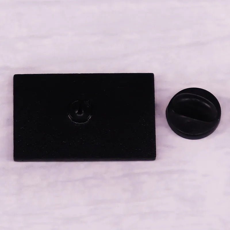 A sleek black rectangular object with a central round indentation sits beside a small, round black piece—perfectly complementing the Progress Pride Flag Enamel Lapel Pin for an inclusive and stylish look.
