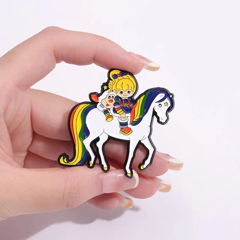 A hand holds the Rainbow Brite Horse - Enamel Pin, featuring a blonde cartoon girl and her white dog riding a white horse with a rainbow mane and tail—perfect for pride and Rainbow Brite fans.