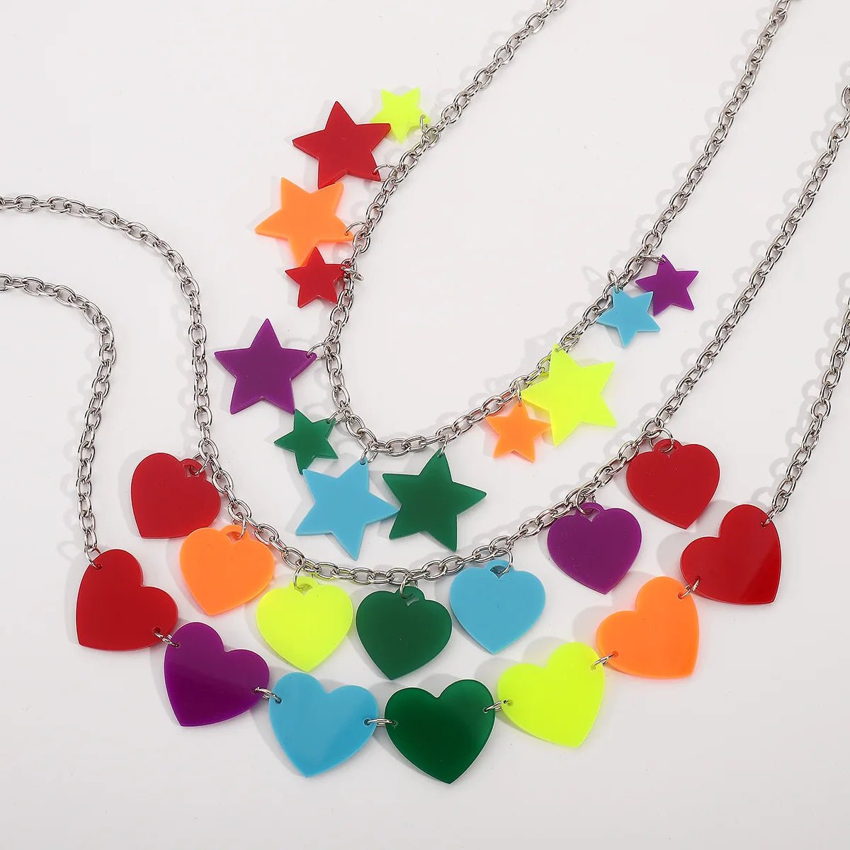 Rainbow Pride Acrylic Necklace - 3 designs: silver chains with colorful acrylic charms—one with rainbow stars, one with love hearts, and one combining both in a gradient. Vibrant pride accessories displayed on a white background.