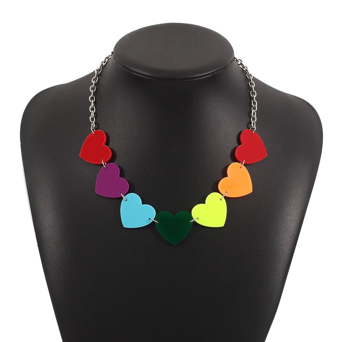 The Rainbow Pride Acrylic Necklace—one of three unique designs—features seven rainbow-colored love hearts on a silver chain, making it a standout pride accessory. Shown displayed on a black mannequin bust.