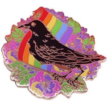 Rainbow pride enamel pin featuring a striking black crow against a rainbow flag surrounded by vivid purple flowers and green leaves