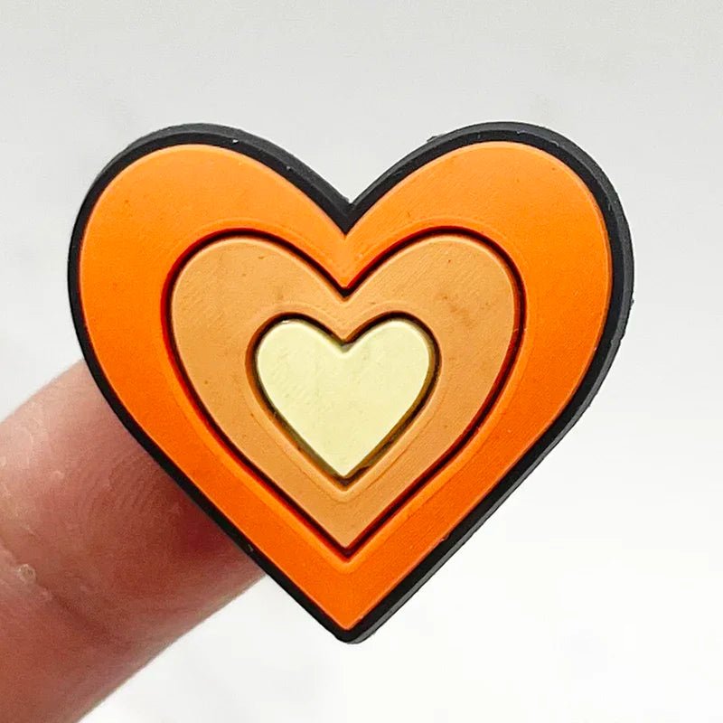 A person holds a Retro Roller Skate theme Shoe Charm, a three-layered heart-shaped object reminiscent of a vintage keepsake, with dark orange, light orange, and cream-colored layers. The charm evokes the allure of an orange jibbitz against a plain white background.