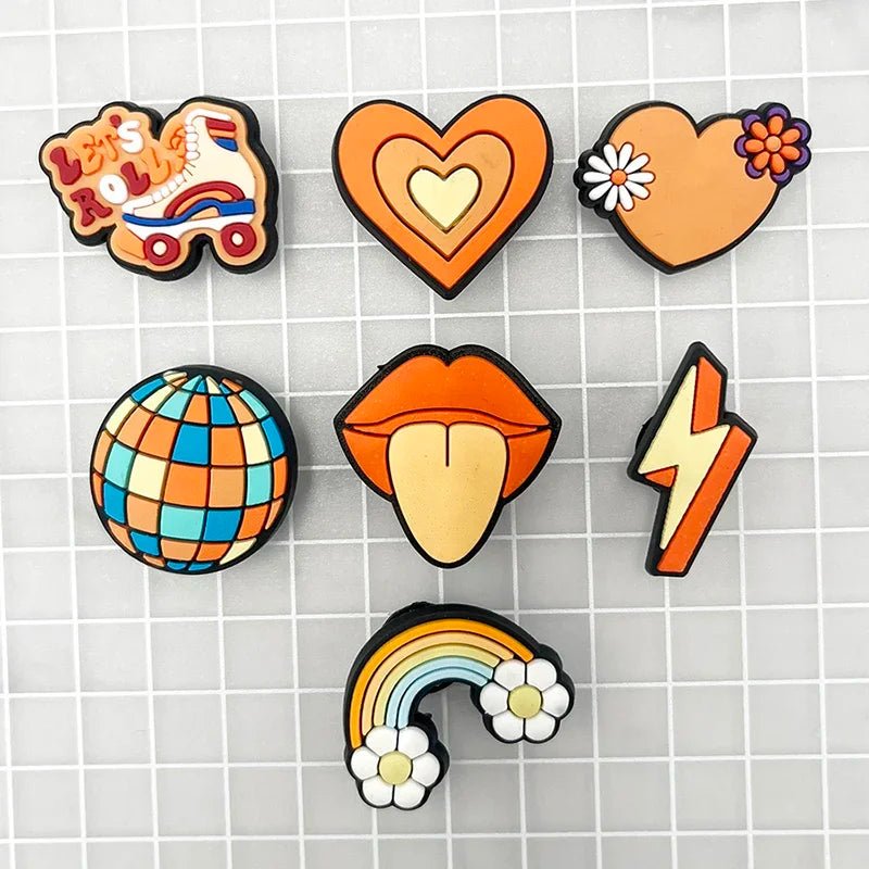 A grid background highlights the retro charm of colorful Retro Roller Skate theme Shoe Charms: a quad skate with "Let's Roll," a heart with a daisy, a disco ball, lips with tongue, an electrifying lightning bolt, and a vibrant rainbow adorned with clouds.
