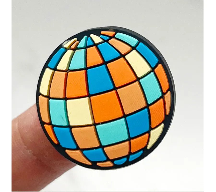 A person holds a small, vibrant spherical object featuring checkered orange, blue, yellow, and turquoise squares, resembling the charm of a Retro Roller Skate theme Shoe Charms.