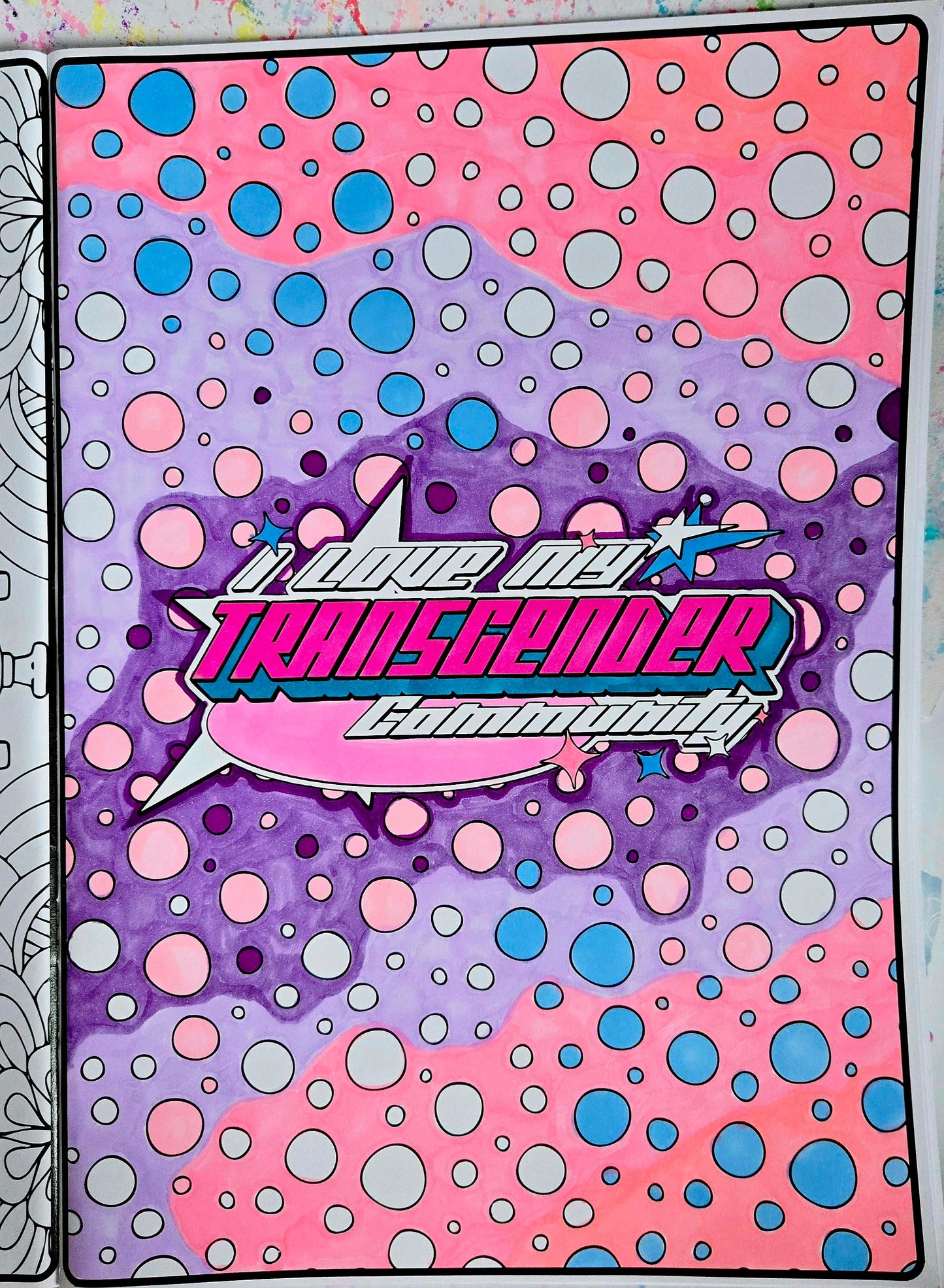 A vibrant page from the Skate Not Hate - Pride Colouring Book features pink, blue, and purple bubbles with bold "I Love My Transgender Community" text, celebrating LGBTIQA+SB pride against a starburst and dotted background.