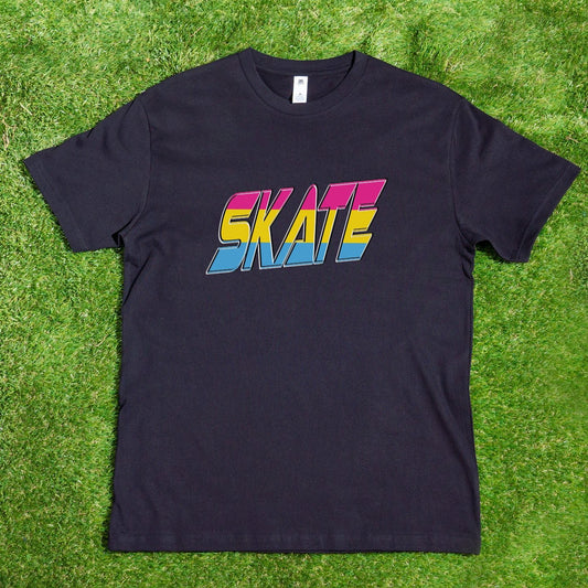 A SKATE Pansexual - Local hand printed t-shirt by My Store, featuring the word "SKATE" in bold, colorful letters with a 1980s retro style, is displayed on a wooden hanger from a tree branch. The scene includes lush greenery and vibrant flowers under sunlight casting beautiful shadows. Custom orders are available to celebrate diversity such as the Pansexual Pride Flag.
