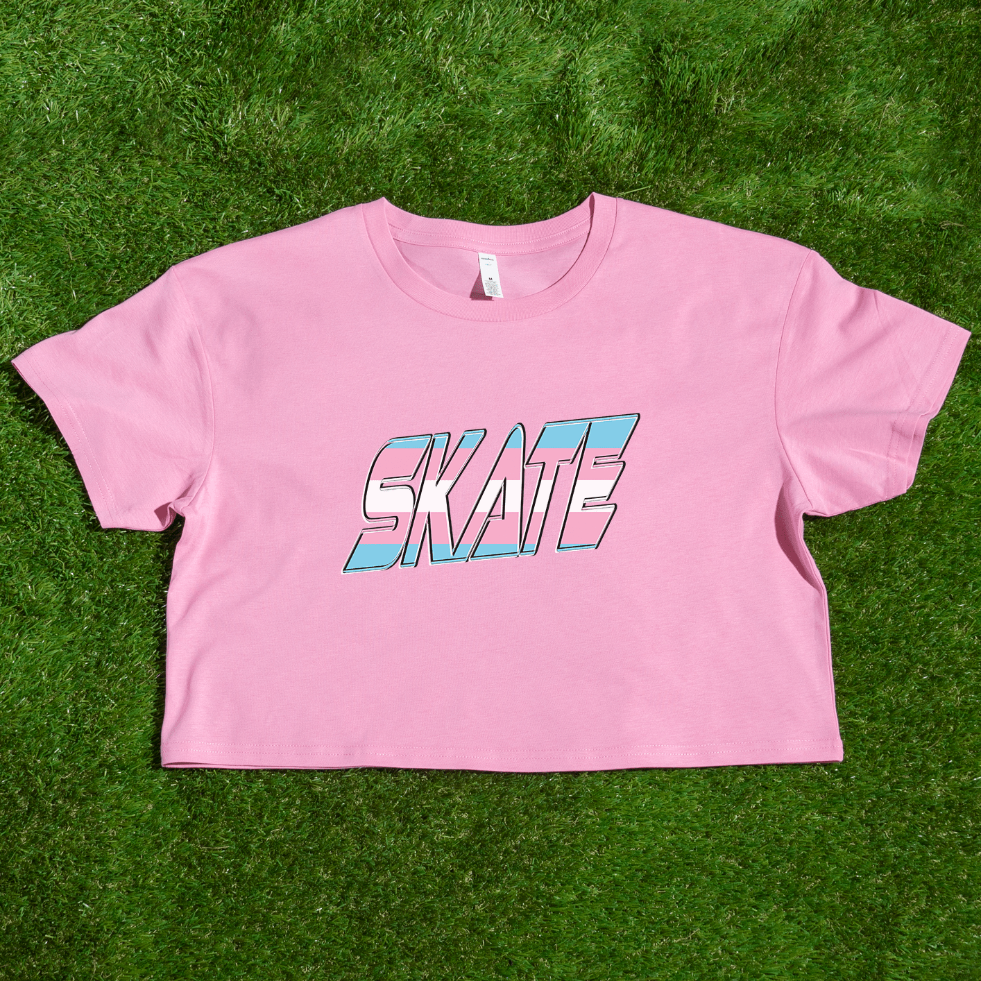 The "SKATE Trans Flag - locally printed crop tee" by Gay Skate is a black T-shirt featuring the word "SKATE" in bold, colorful, and stylized letters on the front. The letters have a gradient effect with shades of pink, blue, and white reminiscent of the transgender flag, giving the design a vibrant and dynamic appearance. The T-shirt has a cropped fit perfect for streetwear fashion.