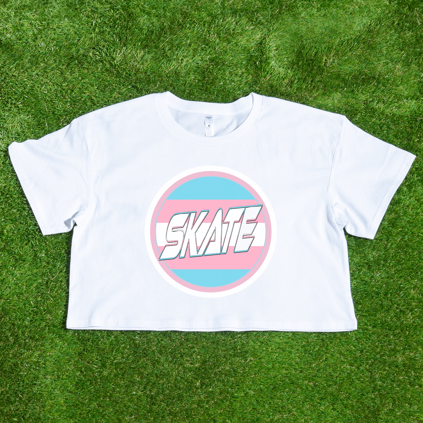 The SKATE Trans Flag round logo - locally printed crop tee by Gay Skate is a black cropped shirt that showcases a round emblem in the center, featuring the word "SKATE" in white stylized text. The emblem is bordered in blue and pink stripes, reminiscent of the trans flag logo, making it a standout piece of queer skatewear.