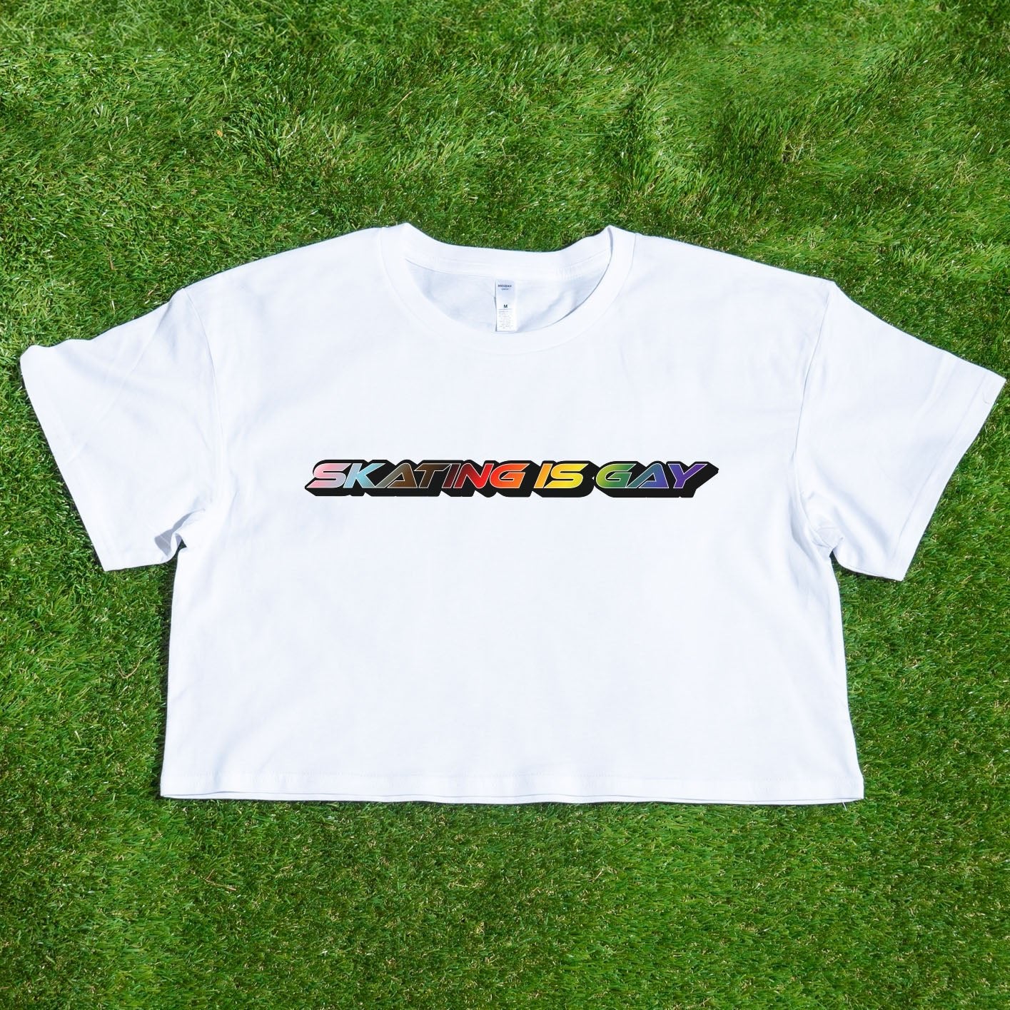 A locally printed crop tee by Gay Skate, featuring short sleeves and a bold "SKATING IS GAY" slogan in rainbow gradient letters across the chest, perfect for celebrating queer skate culture.