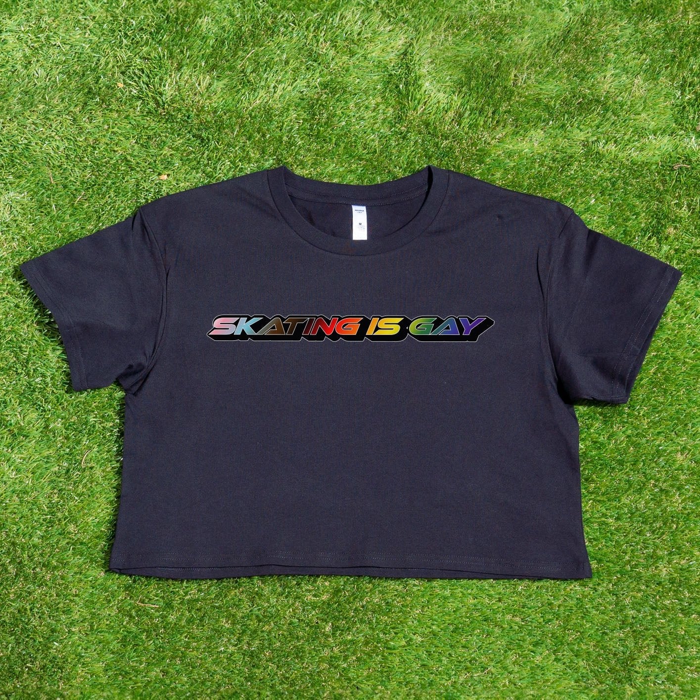 A locally printed crop tee by Gay Skate, featuring short sleeves and a bold "SKATING IS GAY" slogan in rainbow gradient letters across the chest, perfect for celebrating queer skate culture.