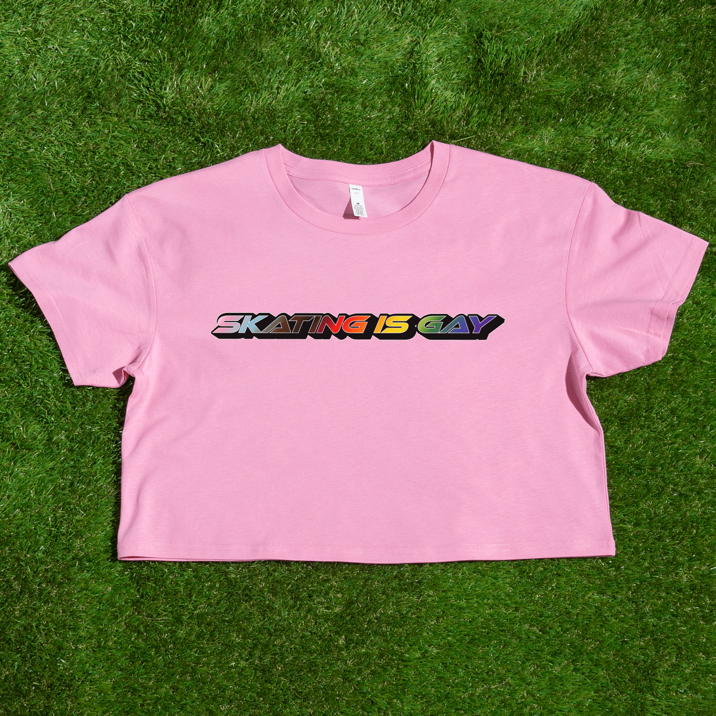 A locally printed crop tee by Gay Skate, featuring short sleeves and a bold "SKATING IS GAY" slogan in rainbow gradient letters across the chest, perfect for celebrating queer skate culture.