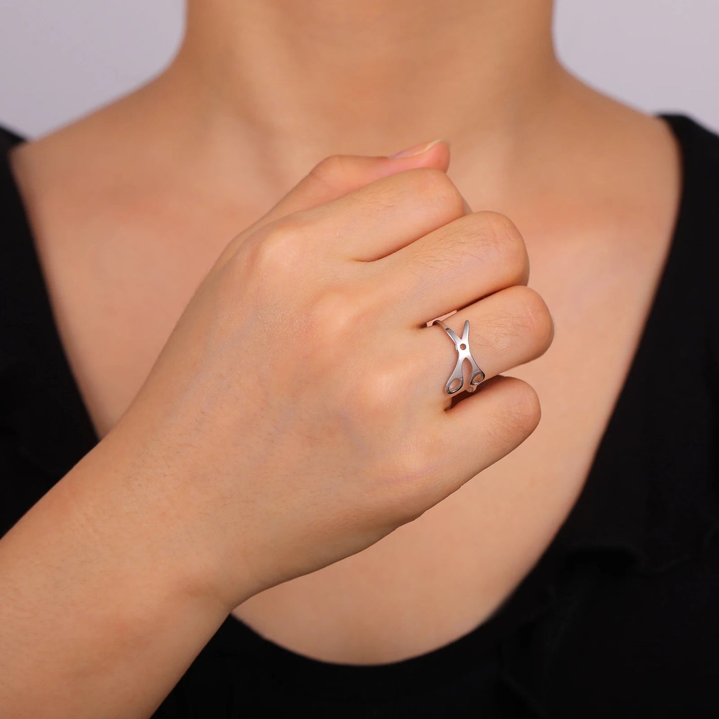 A person wears the Stainless Steel or Gold Scissor Ring - Sapphic, WLW and Lesbian Pride on their middle finger, hand partially closed against their chest. The black top highlights the bold, unique accessory.