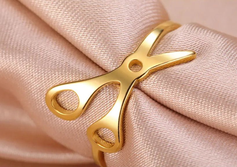 A Stainless Steel or Gold Scissor Ring—Sapphic, WLW, and Lesbian Pride—is showcased on soft pink fabric, making it a perfect addition to your collection of sapphic pride accessories.