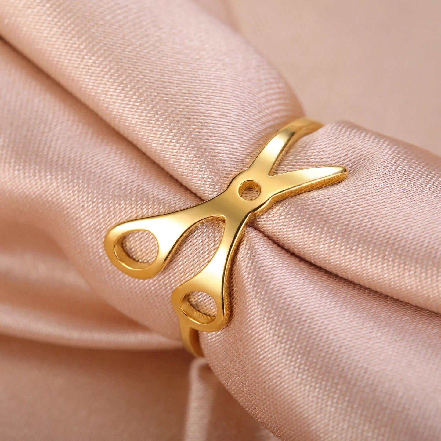 A Stainless Steel or Gold Scissor Ring for sapphic, WLW, and lesbian pride is displayed elegantly on a light pink satin fabric background.