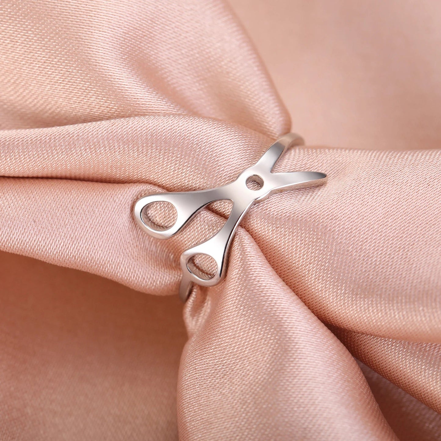 A Stainless Steel or Gold Scissor Ring for sapphic, WLW, and lesbian pride is displayed on light pink satin—ideal for anyone seeking unique pride accessories.