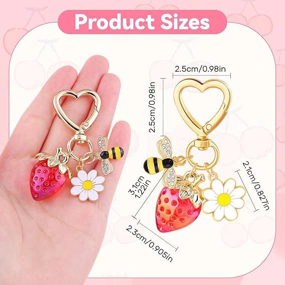 Keychain with strawberry, bee, and flower charms held in a hand, with product size measurements on a pink background.