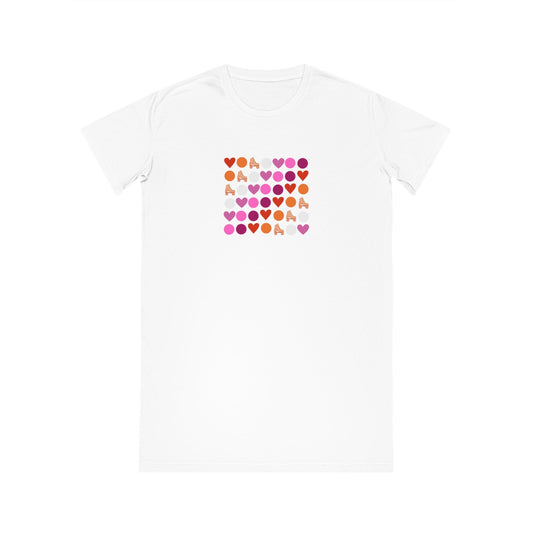 A white Subtle lesbian pride T-Shirt Dress by Printify, made from 100% organic cotton, with a square design on the front featuring a grid of small, colorful hearts in shades of pink, red, orange, and purple. The word "LOVE" is spelled out in the grid with the hearts.
