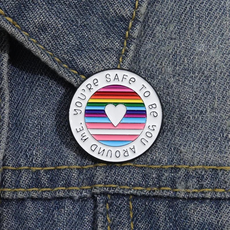 The "You're Safe To Be With Me" enamel ally badge features a white heart on rainbow-striped denim, reflecting the spirit of the Rainbow pride flag. Encircled with "You're safe to be you around me," it's an ideal addition to your pride collection.