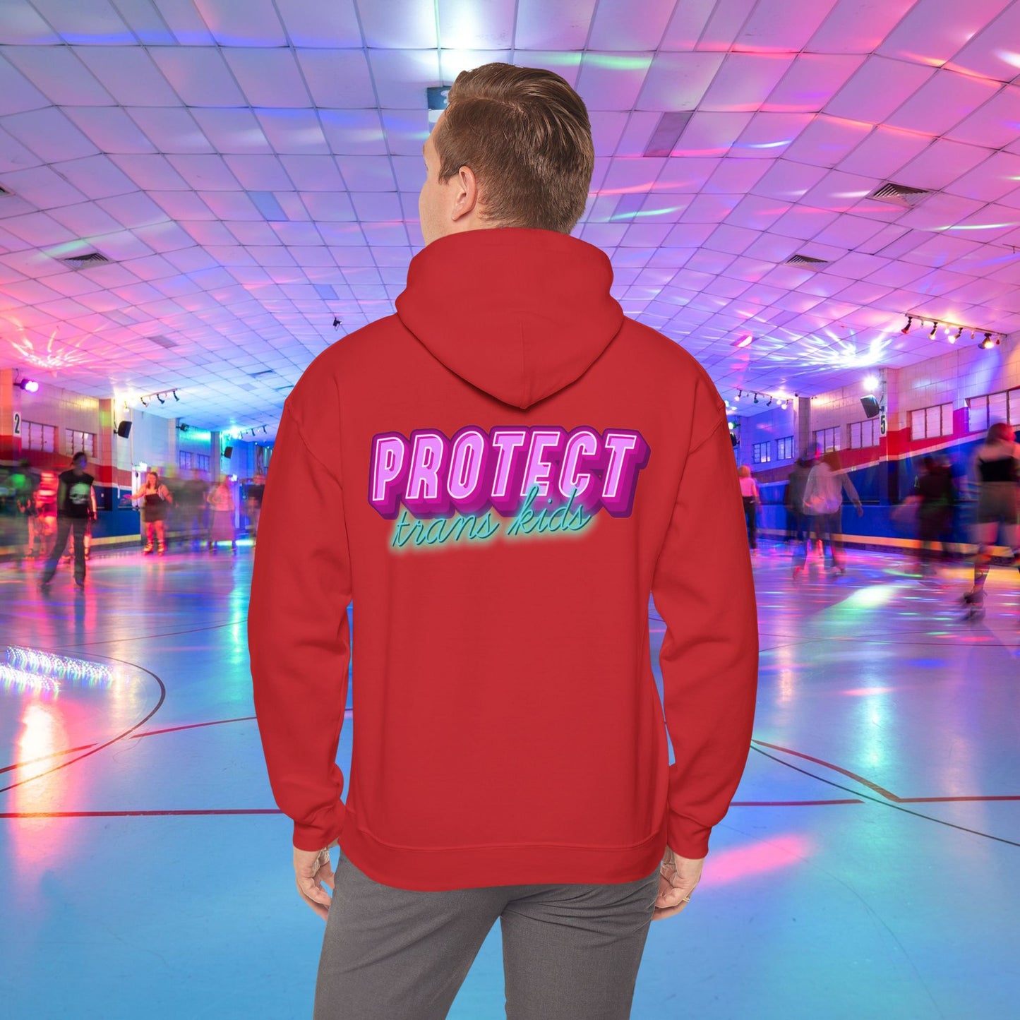 A person is at a roller skating rink, sporting a high-quality Protect Trans Kids Hoodie from Printify, crafted from ethically grown cotton, with "PROTECT trans kids" boldly and colorfully emblazoned on the back. The rink is bathed in vibrant, colorful lights, and other skaters can be seen gliding in the background.