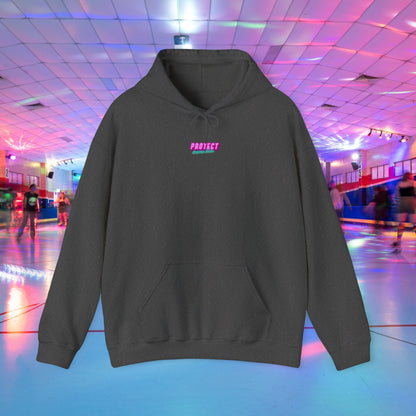 The "Protect Trans Kids" black unisex hoodie with "PROJECT" in pink across the chest is made from ethically grown cotton. It stands out in a dimly lit indoor roller skating rink as colorful lights illuminate the shiny floor.