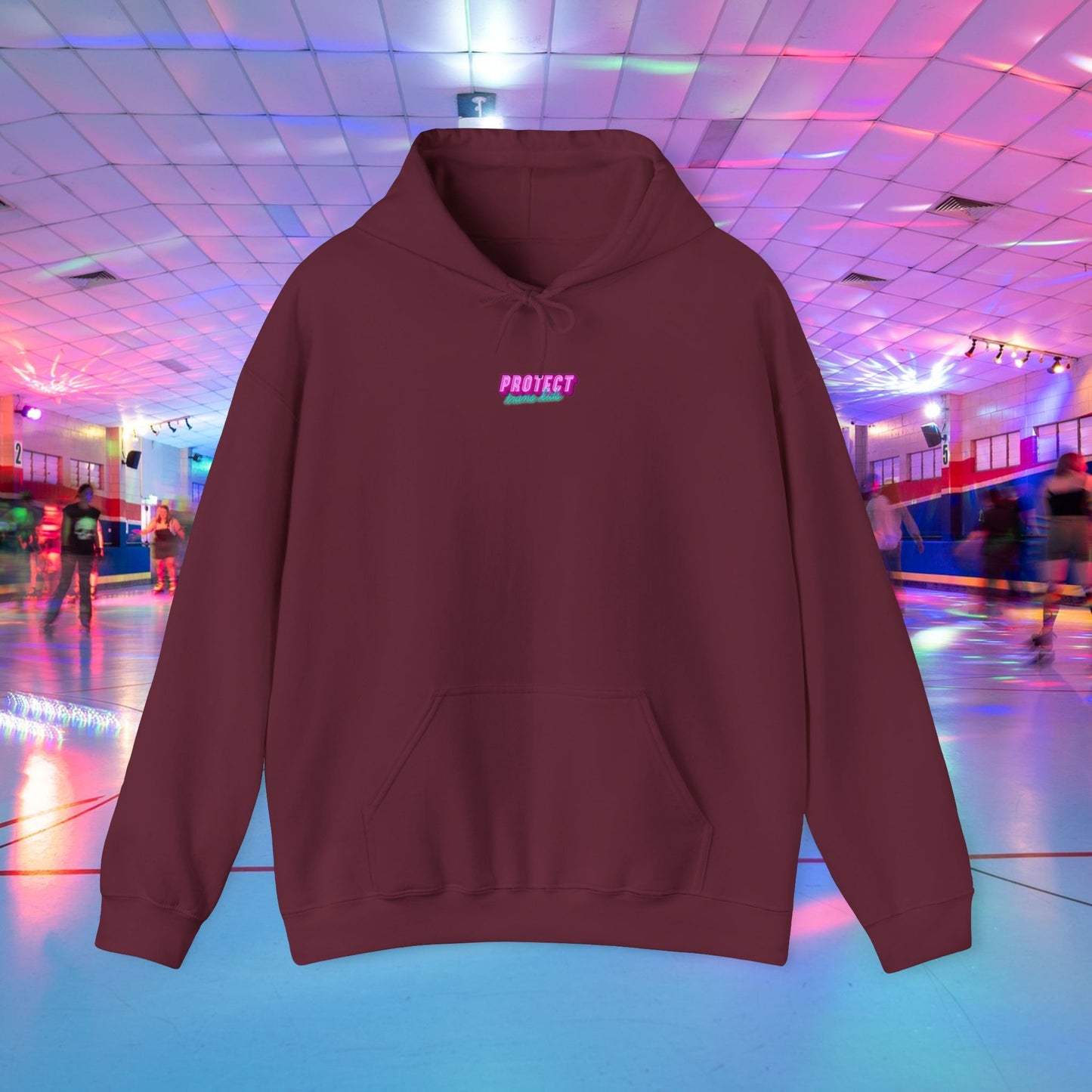 The Protect Trans Kids Hoodie, a maroon unisex piece made from ethically grown cotton with "PROJECT" in pink, is highlighted against a vibrant roller skating rink. The checkered ceiling and neon lights enhance its lively, nostalgic feel.