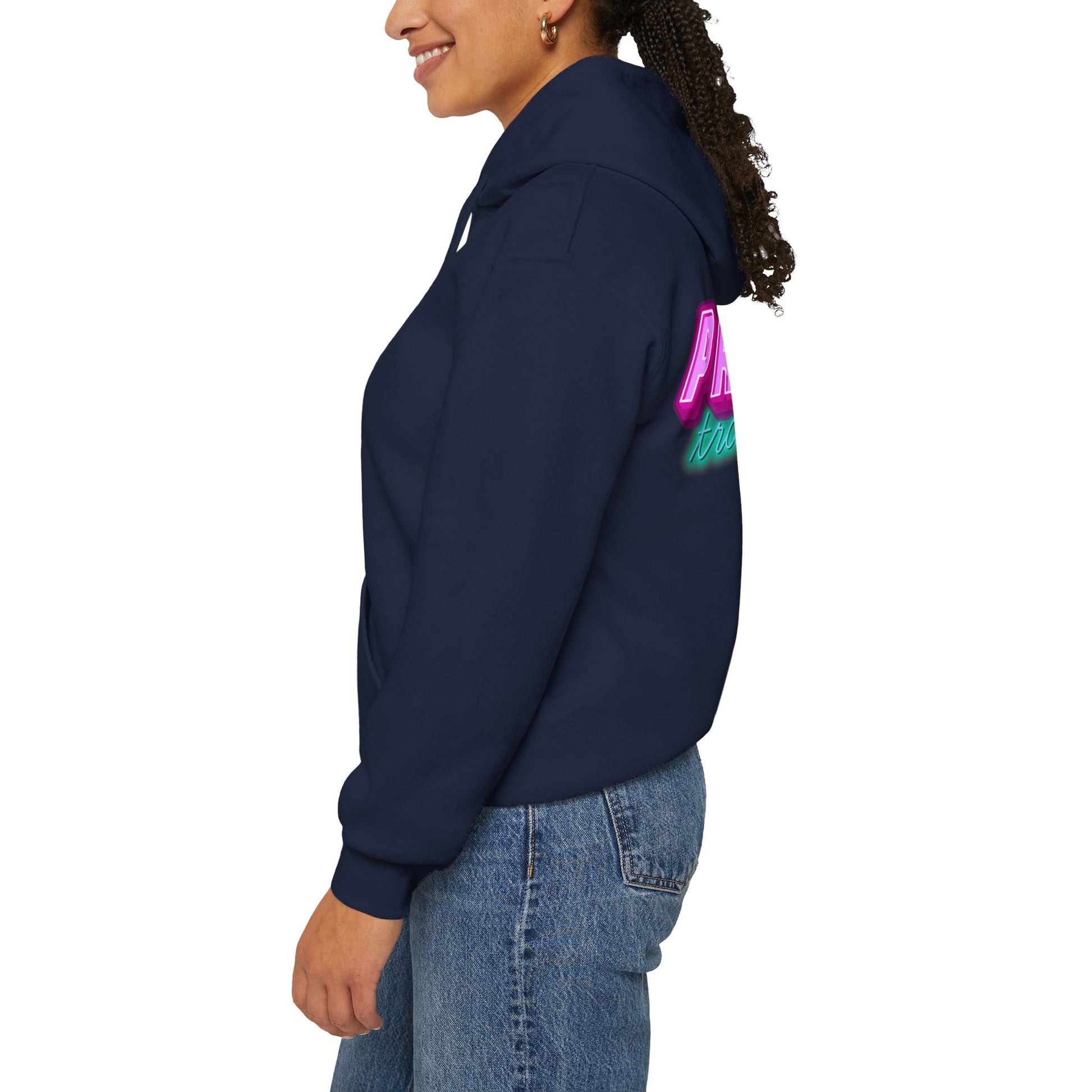 A person wears the "Protect Trans Kids" navy unisex hoodie, made from ethically grown cotton, featuring colorful back text. They pair it with blue jeans, smile sideways with a ponytail against a white background.