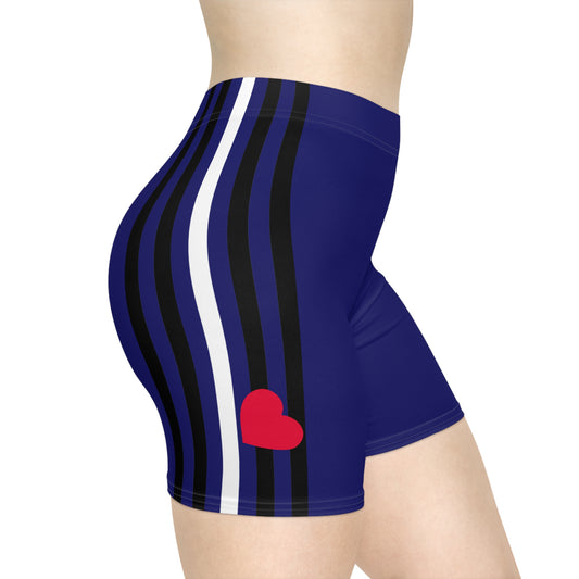 Side view of a person wearing high-waisted, royal blue bike shorts with a unisex design and vertical black and white stripes on the sides. The Leather Pride Flag Bike Shorts by Printify also feature a small red heart on the lower right side, and the person's torso and legs are partially visible.