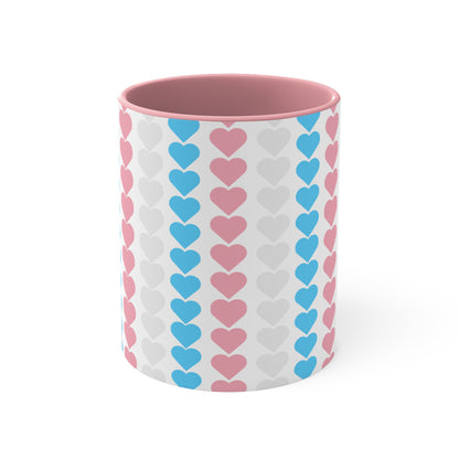 The Trans pride flag love hearts colourful accent mug by Printify features a white exterior adorned with vertical rows of pink, blue, and white hearts, reminiscent of the trans pride flag. Its cheerful and colorful appearance is enhanced by the pink handle and inner rim.