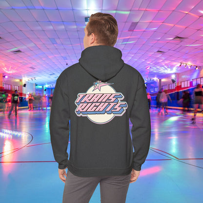 A person wearing a black TRANS RIGHTS Hoodie in trans flag colours - Australian Shipping from GAY SKATE stands in a brightly lit roller skating rink, decorated with colorful lights and occupied by people skating in the background.