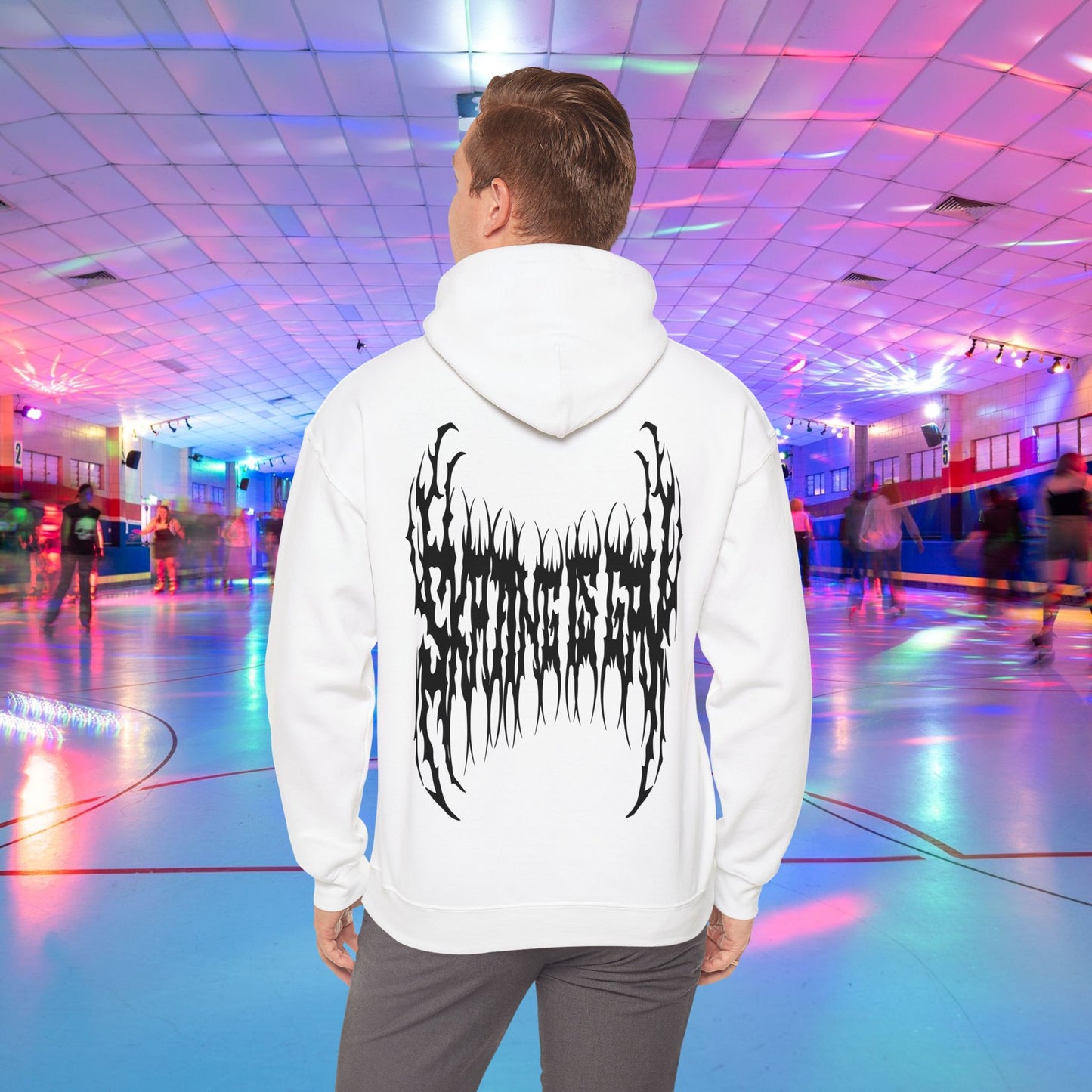 A person wearing the "SKATING IS GAY but make it death metal" hoodie stands in a brightly lit roller skating rink. The rink is adorned with colorful lights, and other people are skating in the background.