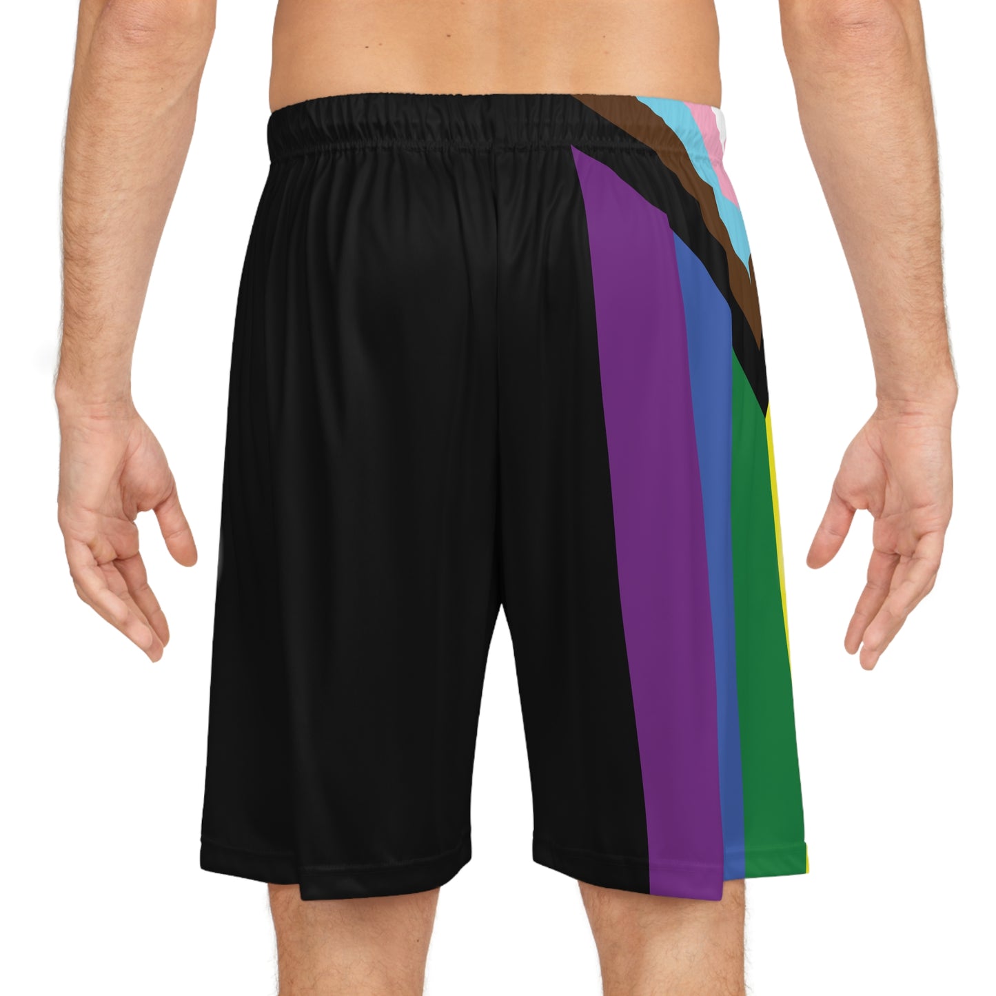 A person is wearing Printify's Progress Pride Rainbow Flag Basketball Shorts made from black, odor-resistant fabric. The shorts feature a vibrant diagonal stripe design in red, orange, yellow, green, blue, brown, black, light blue, pink, and white on the left side. The person's torso is partially visible.