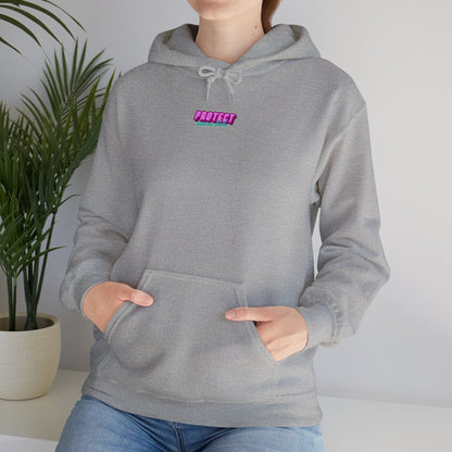 A person wears the "Protect Trans Kids" unisex hoodie, featuring "PROTECT" in pink on a gray backdrop. Made from ethically grown cotton, it has a roomy front pocket. A potted plant adds to the serene setting in the background.