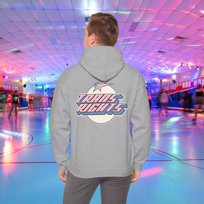 A person wearing a TRANS RIGHTS Hoodie in trans flag colours - Australian Shipping from GAY SKATE stands in a brightly lit roller skating rink, decorated with colorful lights and occupied by people skating in the background.