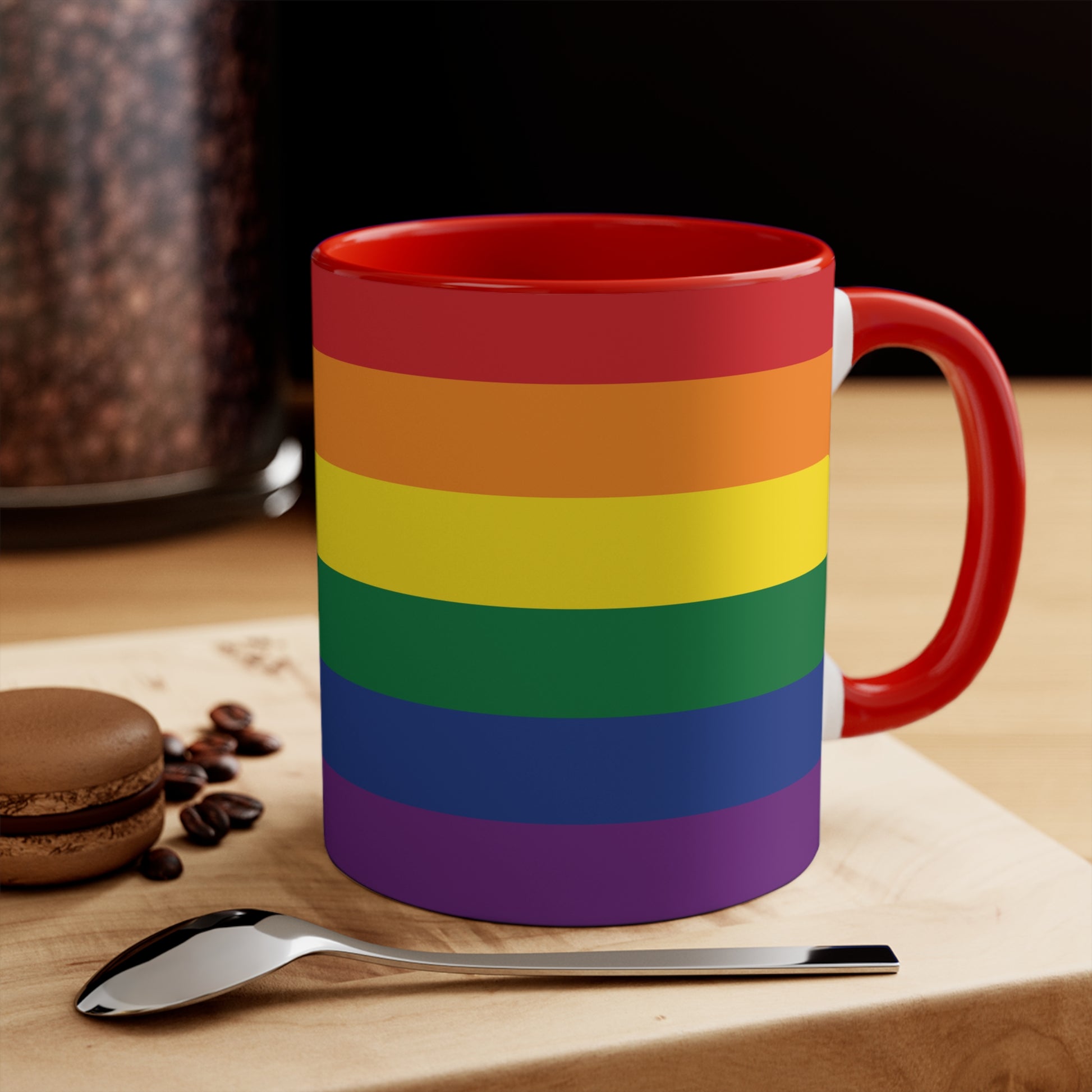 The Rainbow Pride Flag Colorful Accent Mug by Printify is a white ceramic mug featuring a red handle and interior. The exterior showcases horizontal stripes in the vibrant colors of the LGBTQ+ pride flag—red, orange, yellow, green, blue, and purple—offering a striking color contrast.