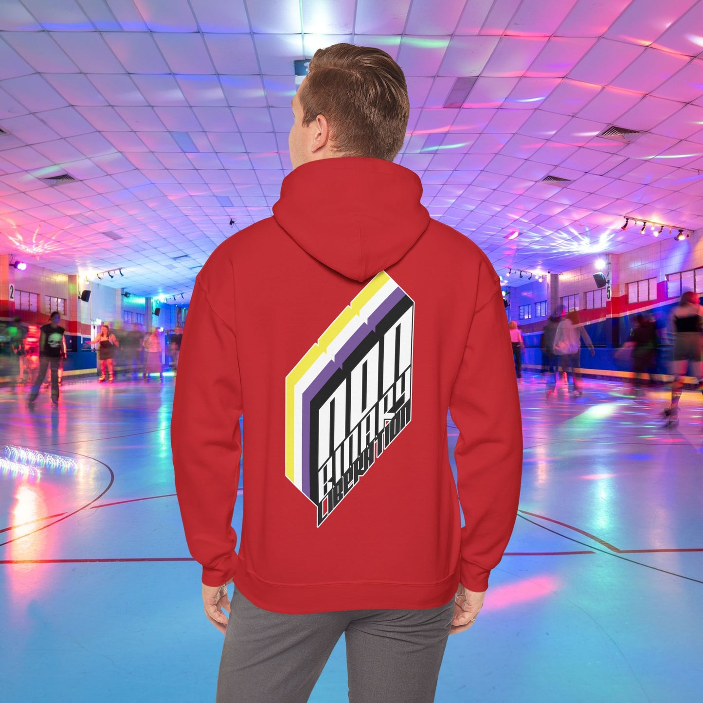 A person wearing the Non-Binary Liberation Hoodie - Australian Shipping by Printify, showcasing a vibrant geometric design on the back in nonbinary pride flag colours, stands in the middle of a roller skating rink. The rink is bathed in vibrant lights of various colors, with several people skating in the background.