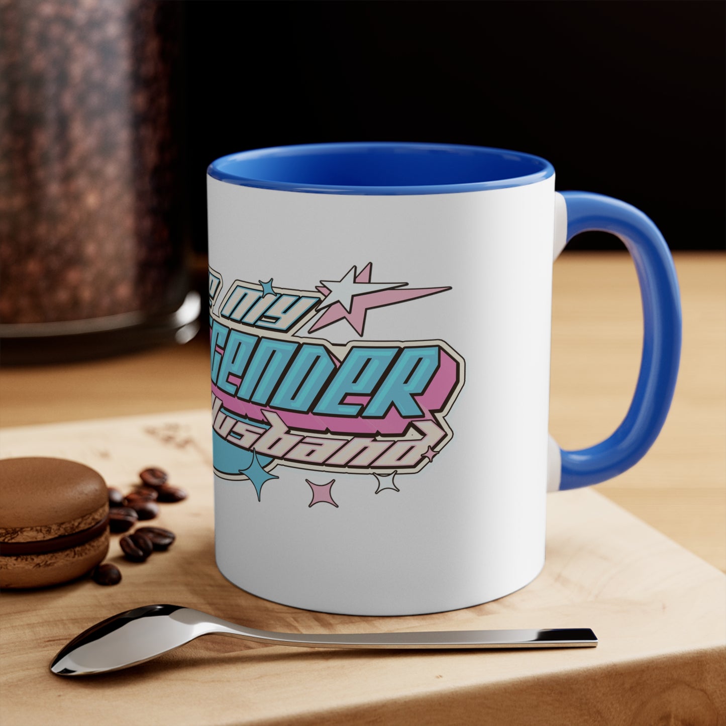 The "I Love My Transgender Husband" original design accent mug by Printify is a white mug with a vibrant interior, featuring bold, retro-styled text. The playful and celebratory design includes stars and geometric shapes in pastel pink, blue, and yellow.